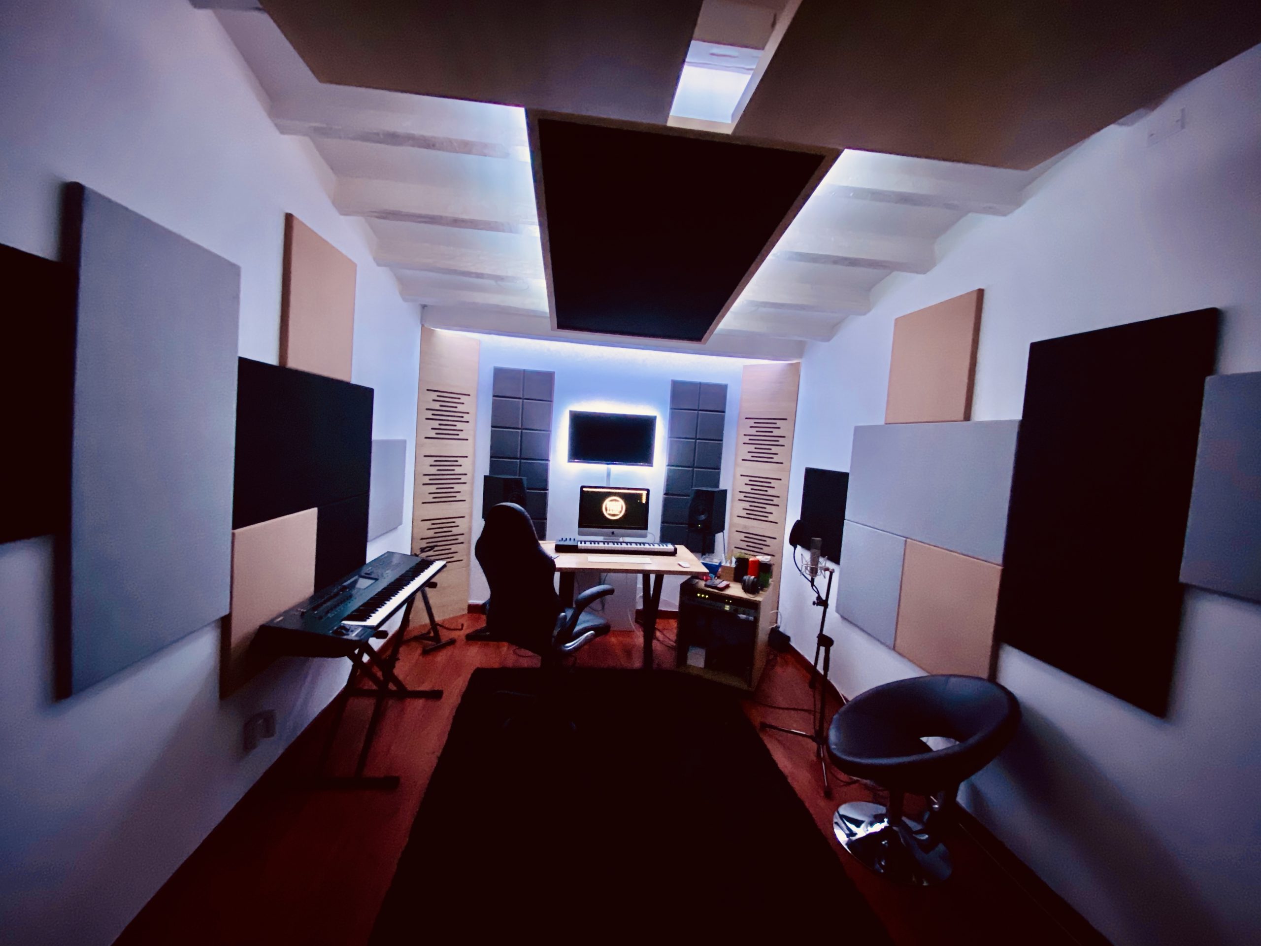 A modern home recording studio with acoustic panels, a computer workstation, and musical keyboard.